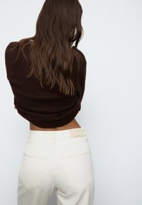 Rjav pulover z teksturirano površino, v kombinaciji z belimi hlačami visokega pasu z oznako na pasu in dvema zadnjima žepoma.