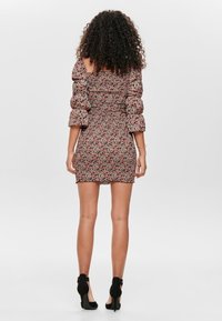 Krótka, dopasowana sukienka z falbanami odkrywającymi ramiona. Kwiatowy wzór w różu i czerni. Teksturowana tkanina z marszczoną górą.
