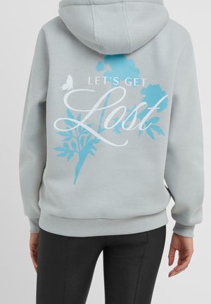 Lichtgrijze hoodie met blauw bloemmotief en witte tekst "LET'S GET Lost" op de achterkant, gedragen door een persoon met zwarte broek.