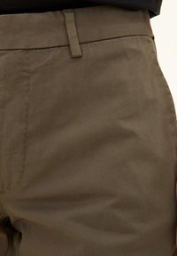 Pantaloni marroni a taglio dritto con una texture liscia, caratterizzati da una vita piatta, passanti per cintura e dettagli di cucitura sottili.