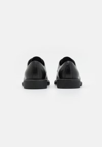 Scarpe in pelle nera con finitura liscia, punta rotonda, suola piatta in gomma e dettagli di cucitura minimali sulla parte superiore.
