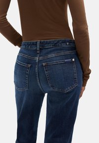 Ciemnoniebieskie dżinsy z denimu z lekko wyblakłym wykończeniem, w fasonie z pięcioma kieszeniami i wysokim stanem. Materiał ma gładką fakturę i subtelne detale przeszyć.