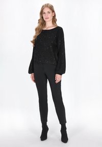 Zwarte, gemêleerde gebreide trui met een ronde hals en ballonmouwen, gecombineerd met zwarte slim-fit broek en enkellaarzen.