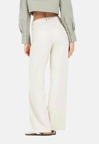 Wide-leg trousers in creamy white fabric, featuring a high waist, clean lines, and a smooth texture. Button detailing on the back pockets.