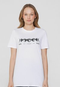 Camiseta de algodón blanca con un estampado gráfico de fases de la luna en negro. Cuello redondo, mangas cortas, corte relajado y textura suave.