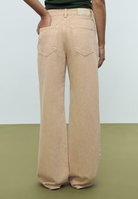 Breda benbyxor i ljus persikofärgad denim, med bakfickor och hög midja. Texturerad tyg med sömdetaljer och ett märke baktill.