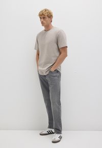 Gray striped t-shirt with short sleeves, paired with faded gray jeans and three-striped sneakers. Model standing with hands in pockets.