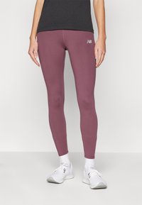 Sportovní legíny v tlumené mauve barvě, s hladkou texturou a jemným logem na stehně, v kombinaci s bílými sportovními botami.