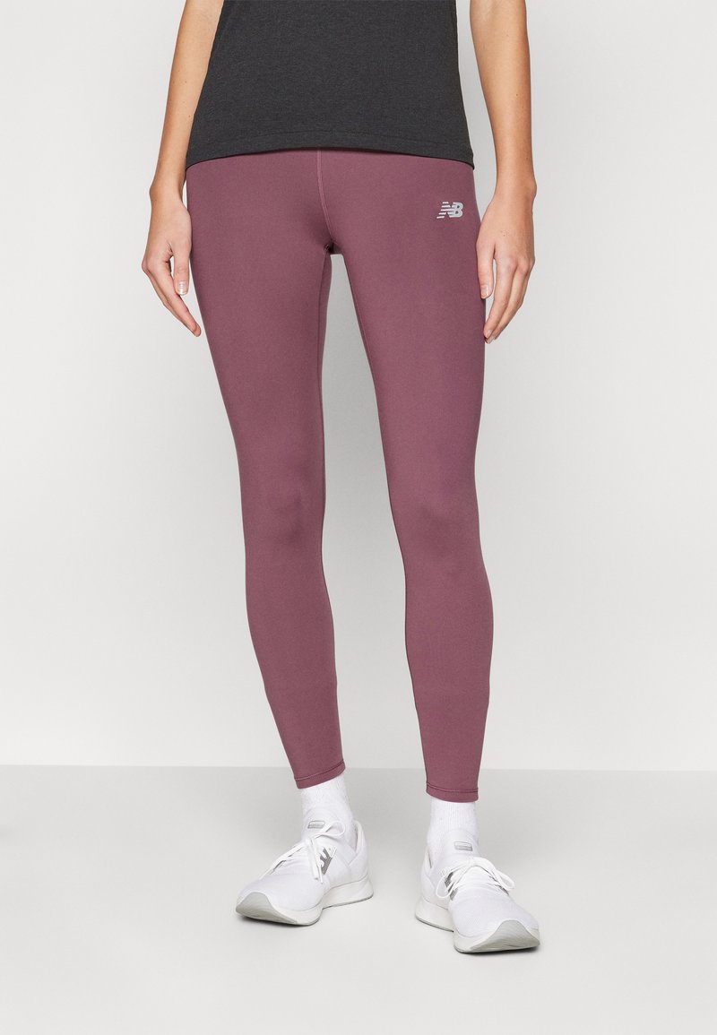Sportovní legíny v tlumené mauve barvě, s hladkou texturou a jemným logem na stehně, v kombinaci s bílými sportovními botami.
