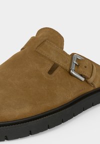 Καφέ καστόρινη γόβα τύπου κλογκ με ρυθμιζόμενο ασημένιο λουράκι και παχιά μαύρη ελαστική σόλα.