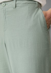 Lichtgroene linnen broek met een gladde textuur, knoopsluiting en zijzakken. Eenvoudige, relaxte pasvorm met stikseldetails.