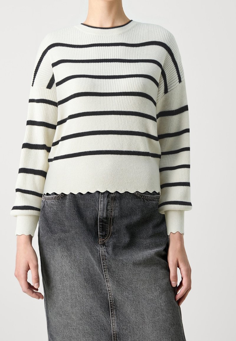 Pull rayé côtelé en écru et bleu marine, avec un ourlet festonné et des épaules tombantes, associé à une jupe en denim foncé.