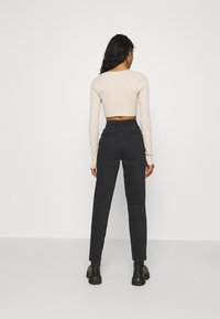 Beżowy krótki top z długim rękawem połączony z czarnymi spodniami wysokiej talii. Spodnie mają standardowy krój i elastyczny pasek w pasie, z czarnymi botkami.