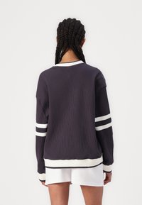 Sudadera de canalé navy con rayas blancas en las mangas y el escote, que presenta un corte relajado y un dobladillo curvado en la cintura.