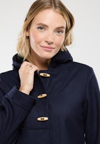 Cappotto con cappuccio blu navy, dotato di bottoni a toggles in legno, con motivo trapuntato e texture liscia. Presenta un collo alto e tasche laterali.