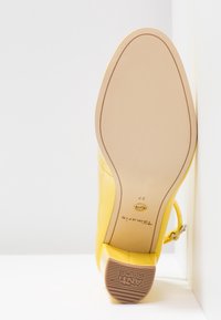 Chaussure à talon jaune inclinée vers le haut montrant une semelle beige, taille 37, marque "Tamaris", et talon texturé avec l'inscription "ANTI SLIDE".
