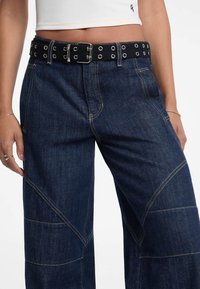 Denim wijde broek met contrasterende gele stiksels, voorzien van een zwarte taille met riem en metalen eyelets, met een gestructureerde afwerking.