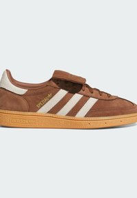 Hnedé semišové tenisky s krémovými pruhmi, okrúly špičkou, gumovou podrážkou a polstrovaným jazykom. Názov značky "adidas" a "SPEZIAL" v zlatých akcentoch.