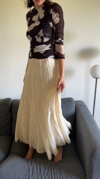 Haut noir à manches longues avec un motif floral blanc, associé à une jupe maxi en dentelle ivoire fluide avec des détails complexes et des plis.