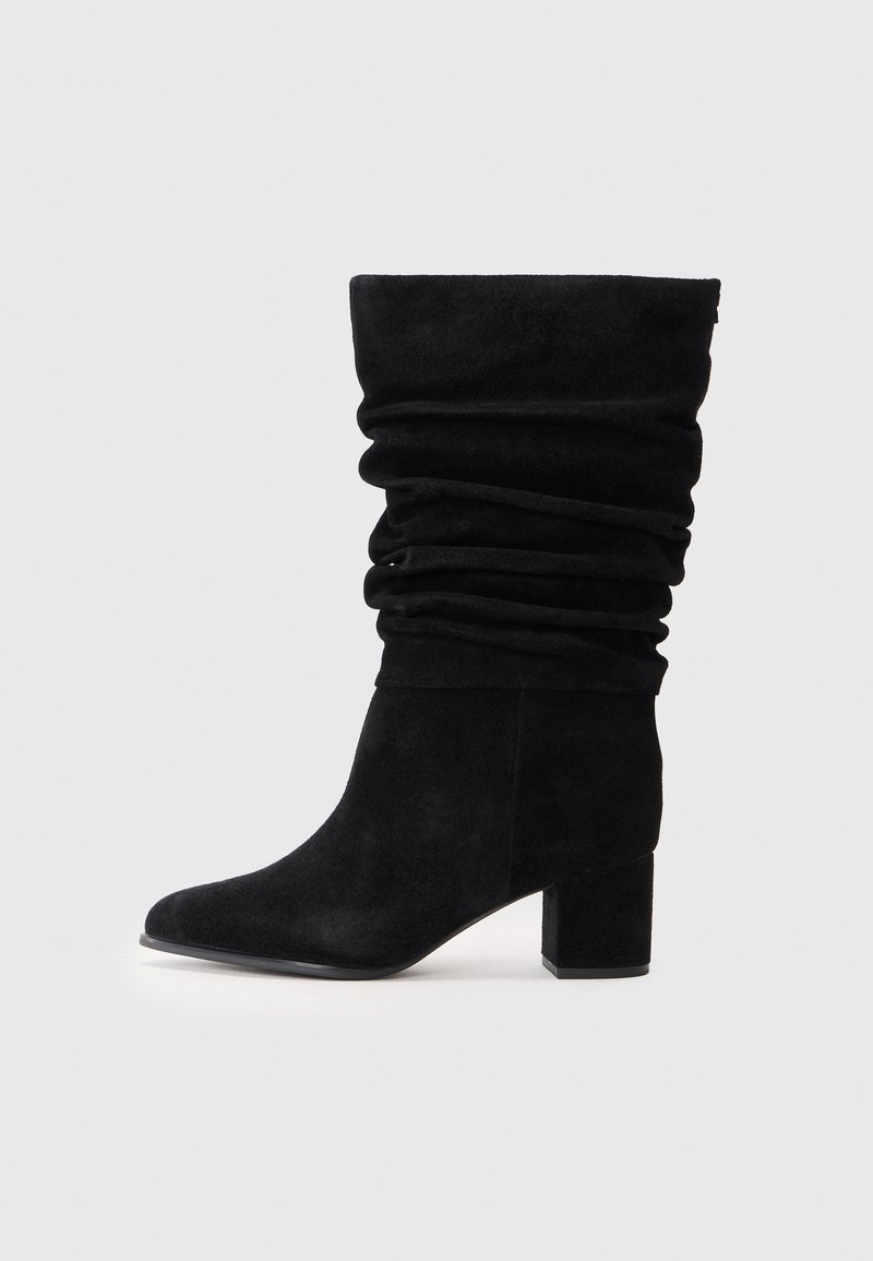 Bottes cheville en suède noir avec un design plissé, orteil pointu et un talon épais. La texture est douce et lisse, sans quincaillerie visible.