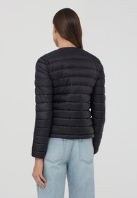 Giacca a vento nera con design trapuntato, attillata e maniche lunghe. Il materiale sembra leggero e resistente all'acqua. Caratterizzata da un collo rotondo.