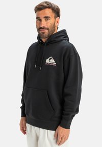 Black hoodie with a large front pocket, drawstring hood, and a graphic logo in grey and pink on the chest. Made from soft material.