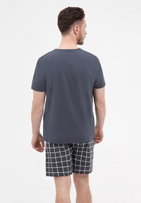 Szary krótki rękaw koszulka wykonana z gładkiego materiału, w połączeniu z w kratkę czarno-białymi szortami, o luźnym kroju i okrągłym dekolcie.