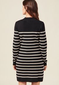 Robe en tricot à rayures noir et blanc avec manches longues et col rond. Présente des poignets et un ourlet côtelés, ainsi qu'une silhouette décontractée et droite.
