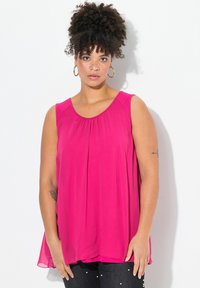 Top sin mangas fucsia con escote redondo y diseño plisado; tejido ligero y fluido con un corte holgado. Combinado con jeans oscuros.