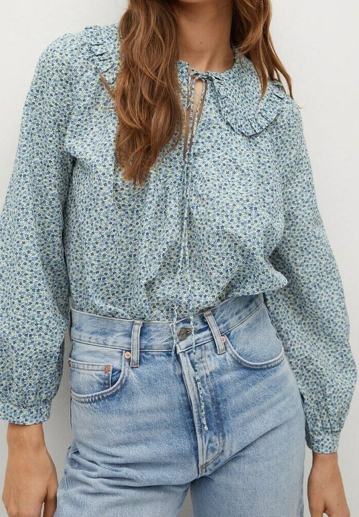 Blumenmuster-Bluse mit Knöpfen, frilltem Kragen, langen Ärmeln und einer Bindeschleife. Hat ein blaues und grünes Muster auf einem hellen Hintergrund.