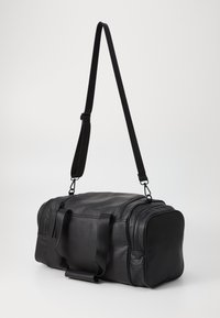 Sac de voyage en cuir noir avec deux poignées et une bandoulière ajustable, doté d'une surface texturée et de compartiments zippés.
