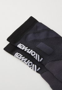 Mangas de compresión en negro y gris oscuro con patrones texturizados y una marca blanca a lo largo del borde, que ofrecen un ajuste ceñido para su uso deportivo.