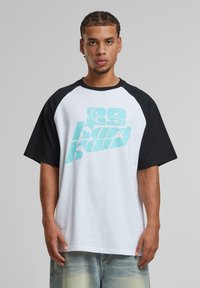 White cotton t-shirt with black raglan sleeves, featuring large turquoise graphic text on the front. Casual fit and short sleeves.