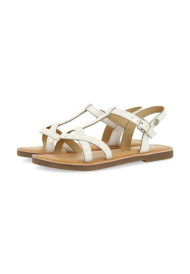 Sandalias de cuero blanco con múltiples correas, hebilla ajustable en el tobillo y suela plana. Presentan una textura suave y un diseño minimalista.