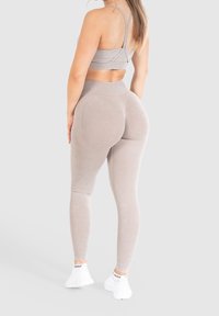 Szary stanik sportowy i pasujące wysokie legginsy z miękkiego, elastycznego materiału. Posiadają bezszwowy design i prążkowaną teksturę. Białe sneakersy.