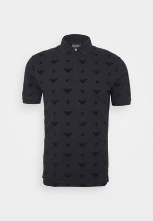 Sort kortærmet polo med krave og knap, der har et mønster af stjerner og ørnelogoer på stoffet.