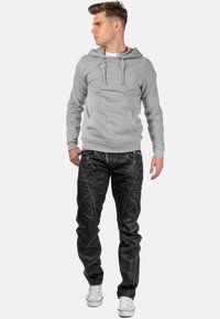 Hoodie gris avec cordons, porté sur un t-shirt blanc. Jean noir avec des détails de couture élaborés et baskets blanches.