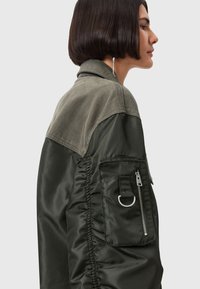 Giacca bomber verde oliva, con una parte superiore in suede, tasca con zip sulla manica, cucitura laterale arricciata e texture contrastanti.