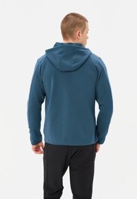 Felpa blu in pile con cappuccio, caratterizzata da una texture morbida, maniche lunghe e un orlo che arriva ai fianchi. Nessun motivo visibile o hardware.