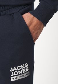 Námorné jogger nohavice vyrobené z bavlnenej zmesi, s bočnou kapsou a bielou potlačou loga "JACK & JONES PERFORMANCE" na stehne.