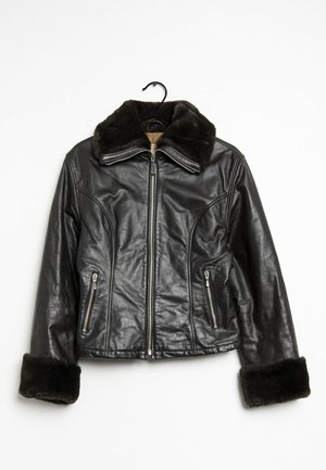 Musta nahkatakki turkiskauluksella ja -hihojen resoreilla, vetoketju edessä ja kaksi vetoketjullista taskua, roikkuu mustassa henkari.