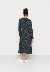 Vestido preto com flores, de mangas longas e corte médio, apresentando pequenos padrões florais multicoloridos. Usado com sapatilhas brancas.