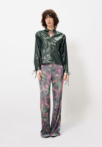 Glanzende groene blouse met lange mouwen en strikdetail bij de hals; gebloemde flared broek in kleuren zoals roze, groen en paars.
