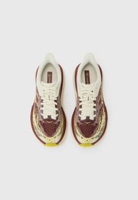 Sportschuhe mit einem bordeauxroten Textiloberteil und einem gelb-blauen abstrakten Muster. Cremefarbene Schnürsenkel und eine strukturierte Sohle.