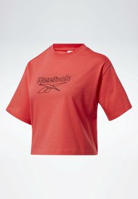 Zkrácený červený bavlněný tričko s krátkými rukávy, na přední straně s černým logem Reebok a kulatým výstřihem. Hladká textura.