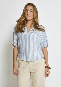 Blusa azzurra chiara a maniche corte con strisce verticali bianche e argentate, caratterizzata da un design a V. Texture liscia, vestibilità ampia e orlo semplice.