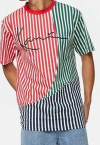 Camiseta a rayas con secciones en rojo, verde y azul marino, con un logo en cursiva; diseño de manga corta y cuello redondo, hecha de tejido suave.