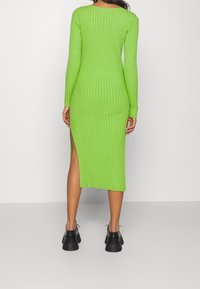 Abito verde a maniche lunghe, a coste, con una fessura laterale, caratterizzato da un design aderente e una morbida texture, abbinato a scarpe nere con lacci.