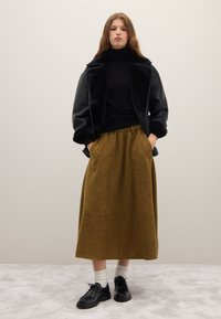 Zwarte faux fur jas, zwarte coltrui en een okergele rok tot op de knie; zwarte schoenen met dikke zolen en witte sokken.