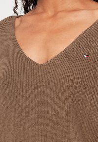 Rudas, juostelėmis megzta palaidinė su V formos iškirpte ir mažu logotipo nuošaliu, kuriame yra raudonos, baltos ir mėlynos spalvos, kairėje pusėje. Minkšta tekstūra.